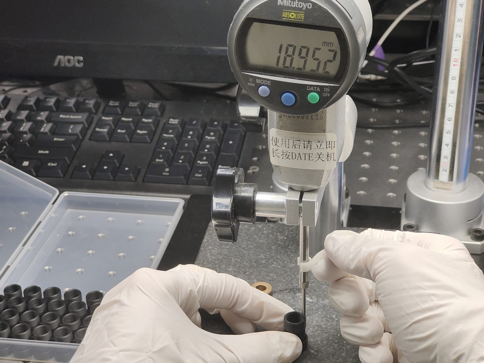 Mitutoyo digital gauge measuring a Lensmind lens barrel at 18.952 mm on the metrology bench